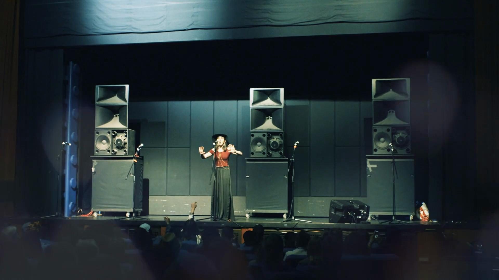 Woman performing on stage with a microphone at the Louder Than A Bomb event coverage shoot by a professional videographer.