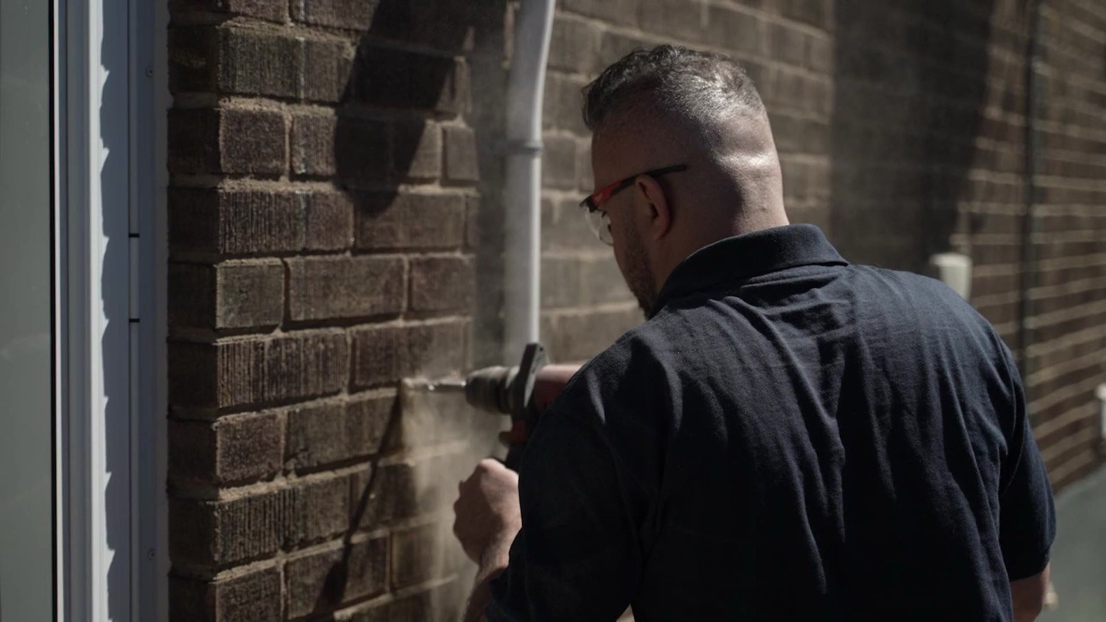 Professional contractor drilling into a dark brown brick wall, captured for Home Repair Spot video production.