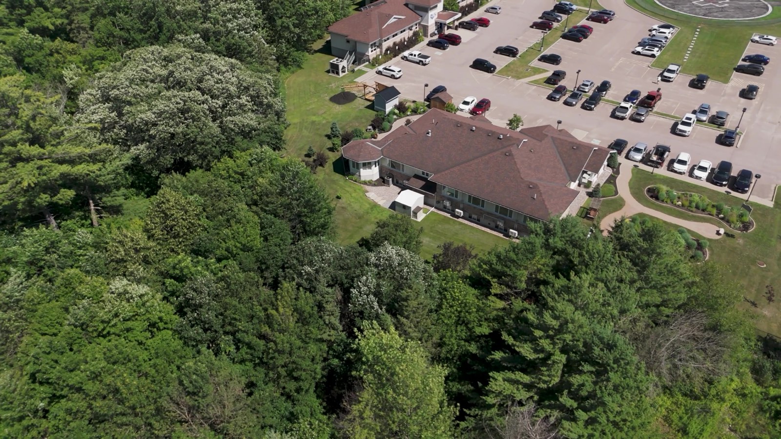 Aerial drone video shot of Renfrew Hospice facility surrounded by parking and lush forest landscape.