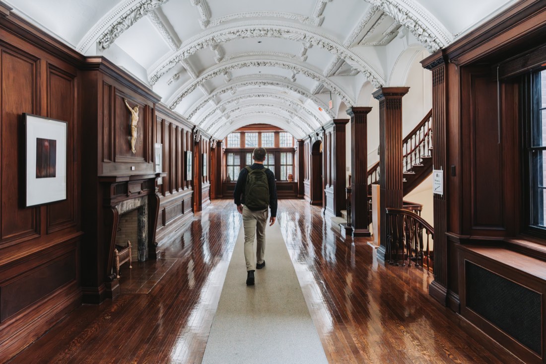 University student with a backpack walking down a classic arched wood-paneled hallway in Toronto.